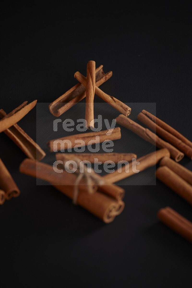 4 Cinnamon sticks stacked and bounded with more sticks in the background on black flooring