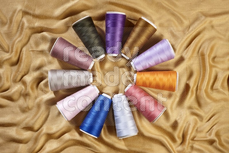 Multicolored sewing thread spools on yellow fabric background