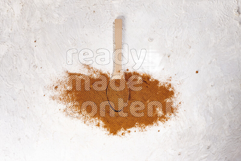 A wooden spoon full of ground paprika powder and surrounded with the powder on white background