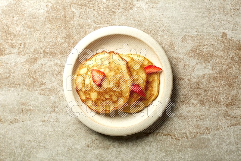 Three stacked strawberry pancakes in a beige plate on beige background