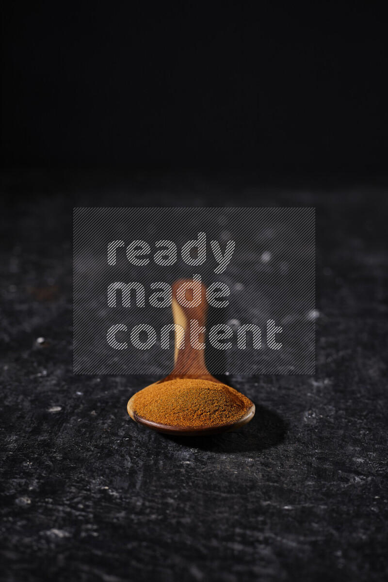 A wooden ladle full of ground paprika powder on black background