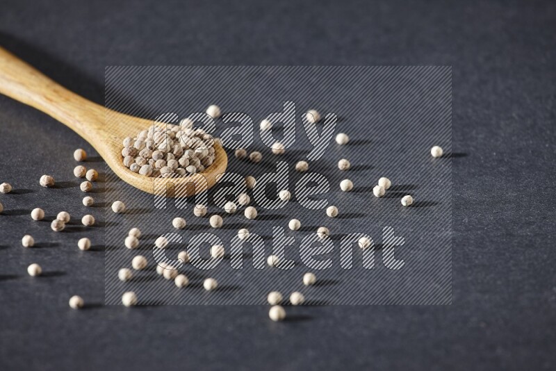 A wooden spoon full of white pepper beads on black flooring