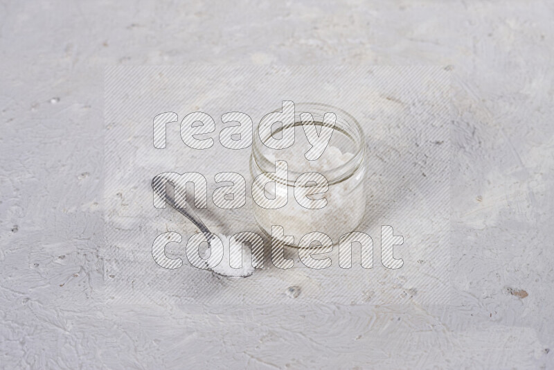 A glass jar full of coarse sea salt crystals on white background