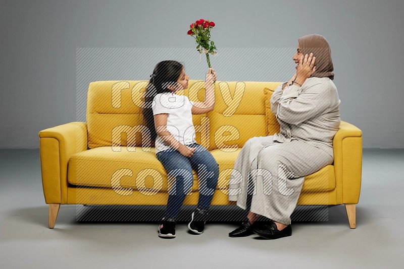 A girl sitting giving flowers to her mother on gray background