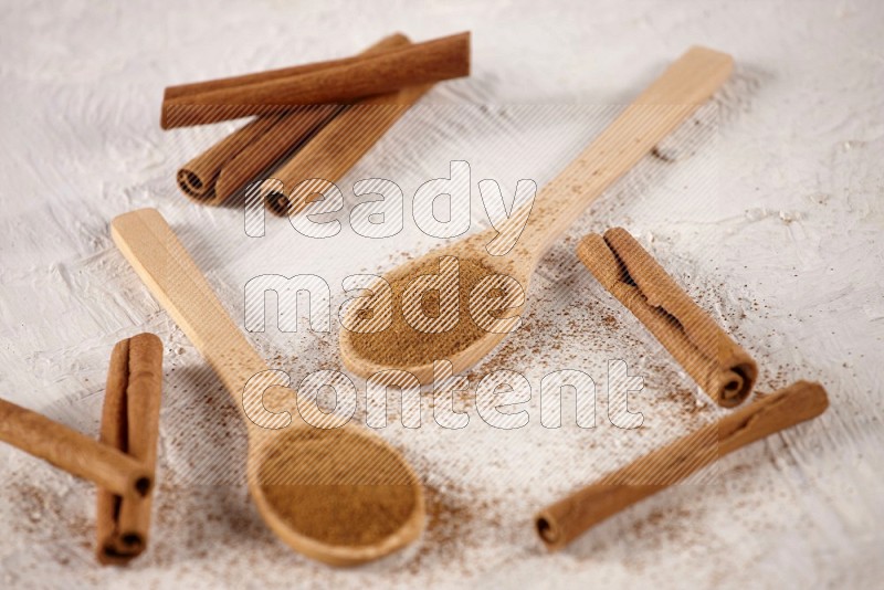 Two wooden spoons full of cinnamon powder with cinnamon sticks on white background