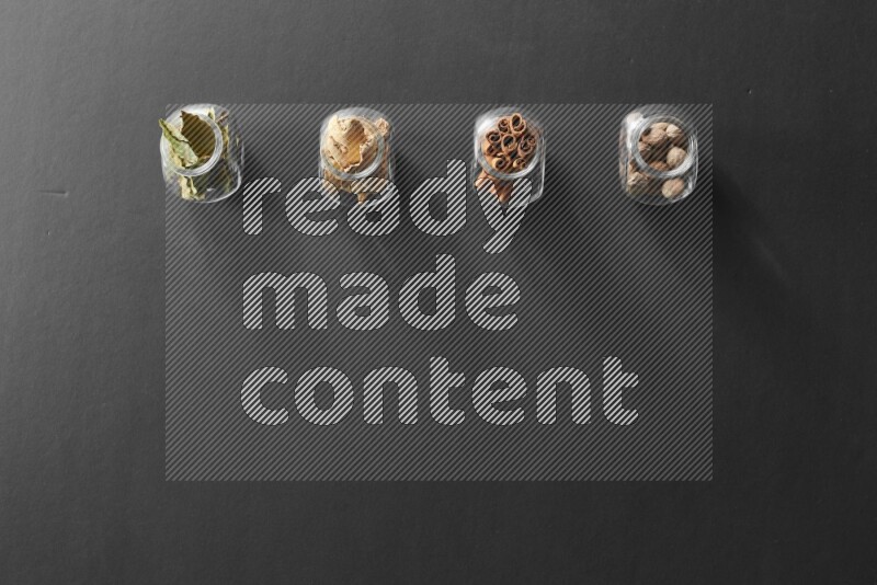 أوراق الغار وزنجبيل مجفف وقرفة وجوزة الطيب في أوعية زجاجية علي خلفية سوداء