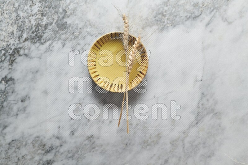Wheat stalks on multicolored pottery plate on grey marble background