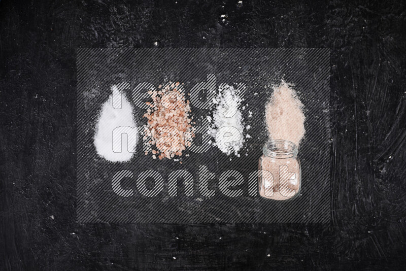 4 glass jars filled with table salt, coarse sea salt, fine himalayan salt and coarse himalayan salt on black background