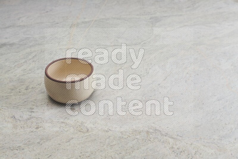 A small beige pottery bowl on grey marble background
