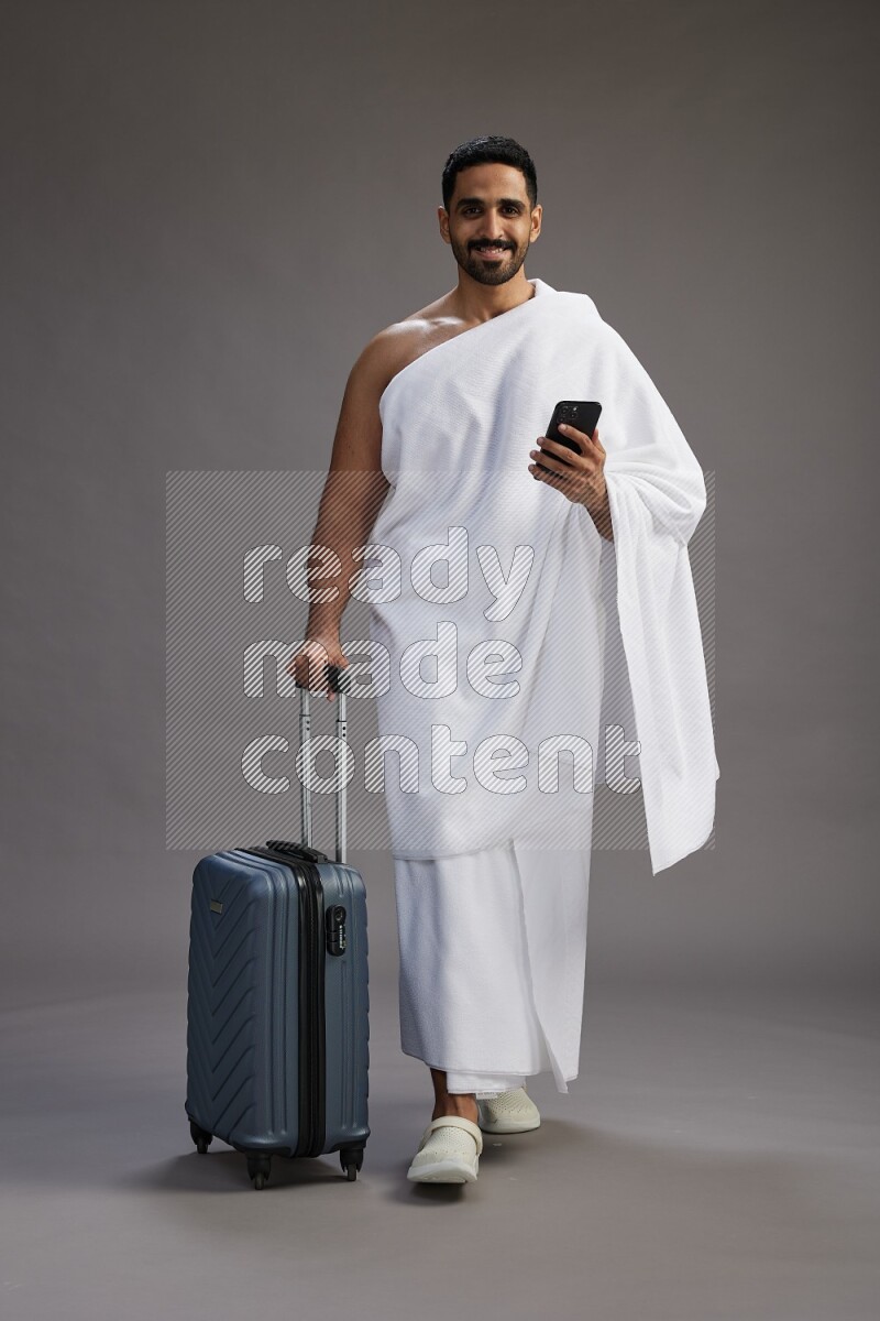 A man wearing Ehram Standing holding traveling bag on gray background
