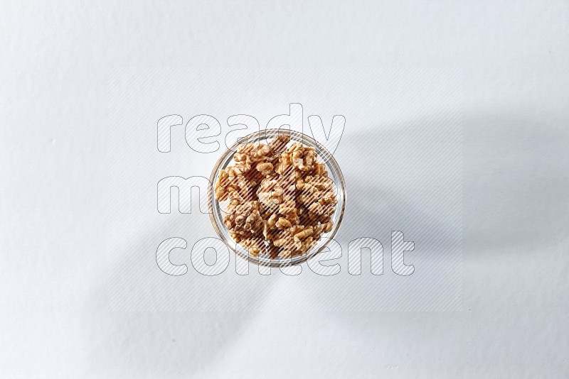 A glass bowl full of peeled walnuts on a white background in different angles