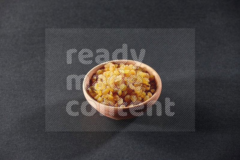 A wooden bowl full of raisins on a black background in different angles