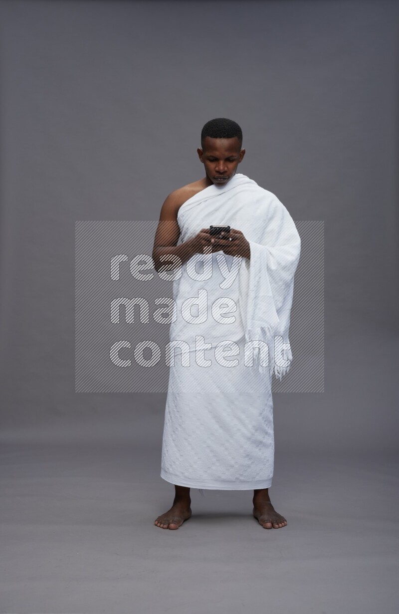 A man wearing Ehram Standing texting on phone on gray background
