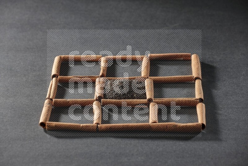 9 مربعات من أعواد القرفة ممتلئة بالشاي في المنتصف محاطة بجوزة الطيب والنعناع المجفف والقرنفل والريحان المجفف والزنجبيل المجفف والقرفة واليانسون والهيل على أرضية سوداء