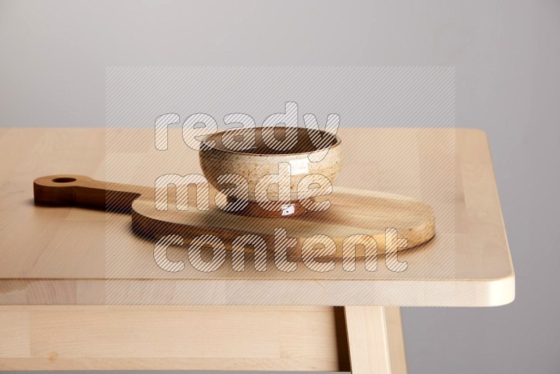 multi colored bowl placed on a  wooden oval cutting board on the edge of wooden table