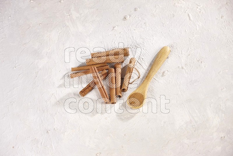 Cinnamon sticks stacked beside a wooden spoon full of cinnamon powder on white background