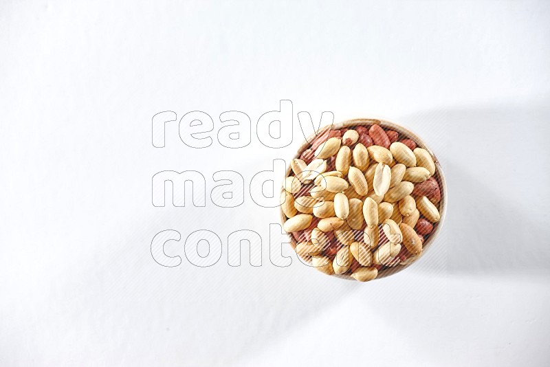 A beige ceramic bowl full of peeled peanuts on a white background in different angles