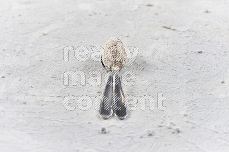 ملعقتان معدنيتان أحدهما ممتلئة ببودرة البصل علي خلفية بيضاء