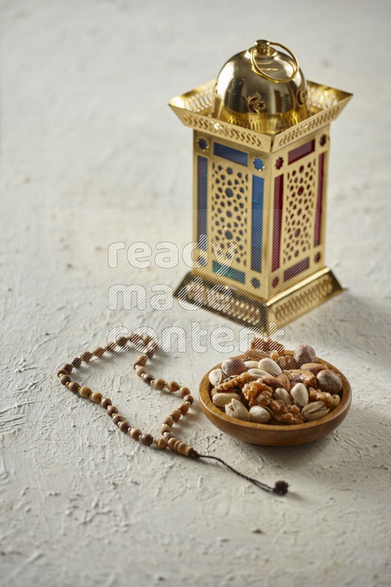 A golden lantern with different drinks, dates, nuts, prayer beads and quran on textured white background