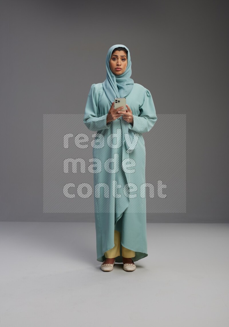Saudi Woman wearing Abaya standing texting on phone on Gray background