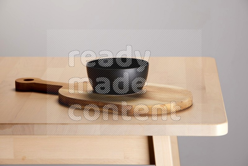 black bowl placed on a  wooden oval cutting board on the edge of wooden table