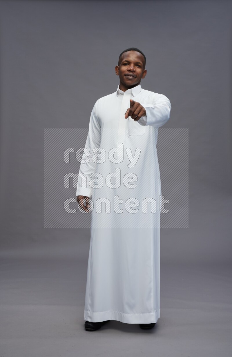 Saudi man wearing thob standing interacting with the camera on gray background