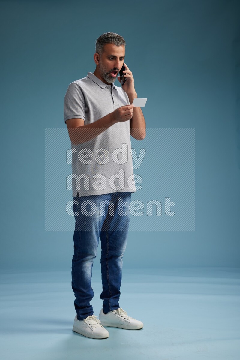 Man Standing holding ATM while talking on phone on blue background