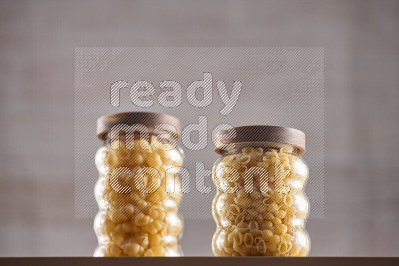 Raw pasta in glass jars on beige background