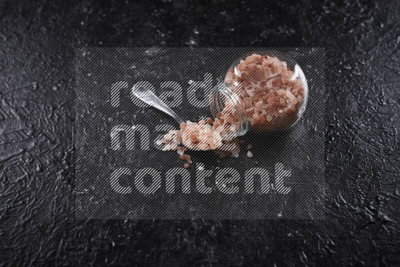 A glass jar full of coarse himalayan salt crystals on black background