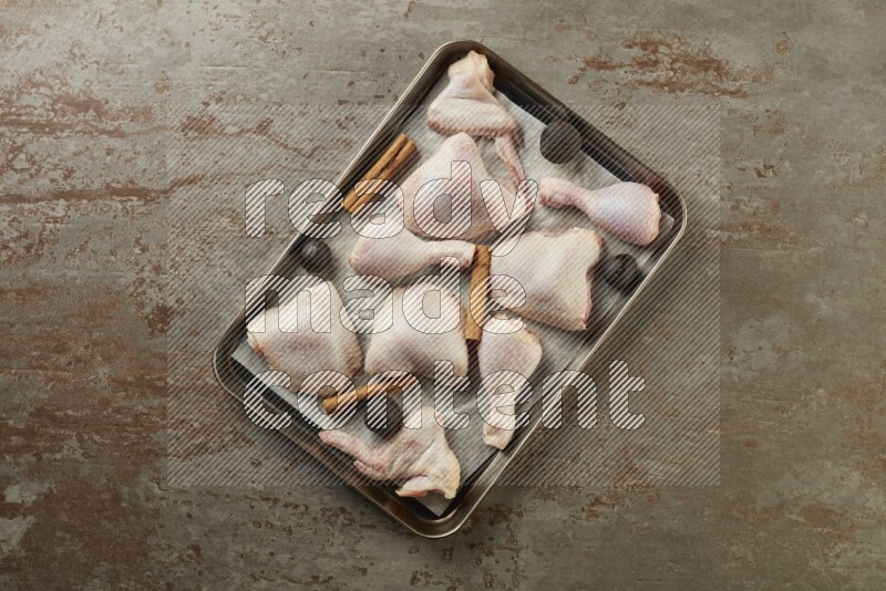 Mixed fresh chicken pieces in an oven tray on a textured rustic background