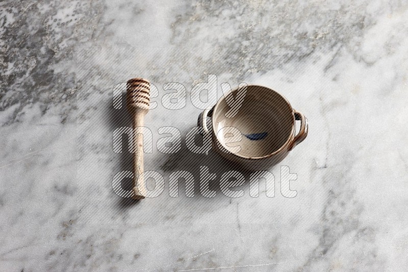 Multicolored Pottery bowl with wooden honey handle on the side with grey marble flooring, 65 degree angle