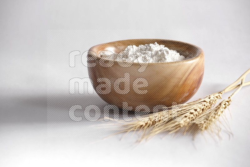 A wooden bowl full of flour with wheat stalks on white background