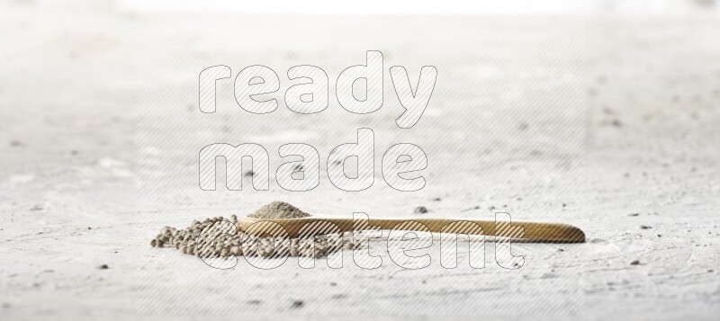 A wooden spoon full of white pepper powder and white pepper beads on textured white flooring