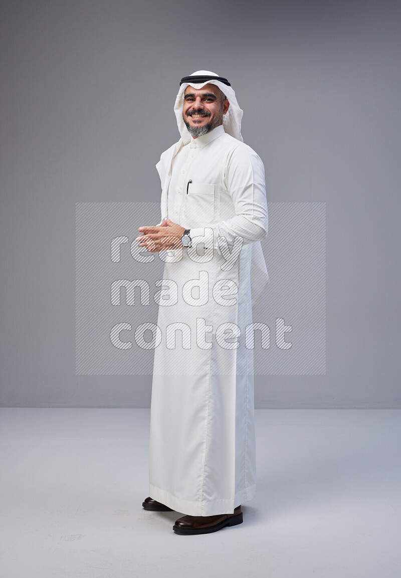 Saudi man Wearing Thob and white Shomag standing interacting with the camera on Gray background