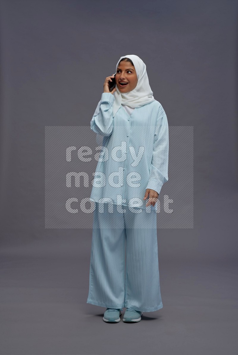Saudi woman wearing hijab clothes standing talking on phone on gray background