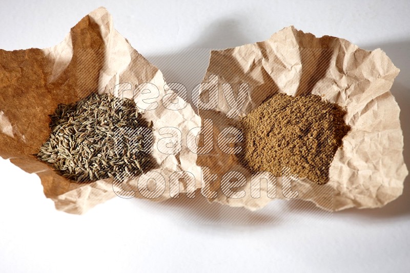 Cumin seeds and cumin powder in 2 crumpled pieces of paper on white flooring