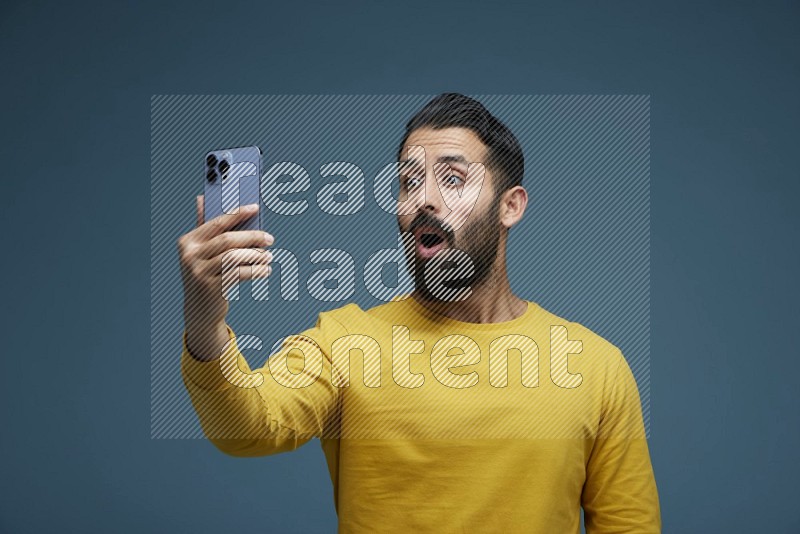 Man Taking a Selfie  in a blue background wearing a yellow shirt