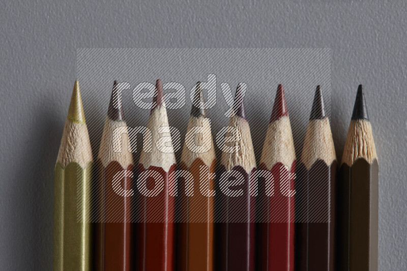 A collection of colored pencils arranged showcasing a gradient of brown hues on grey background