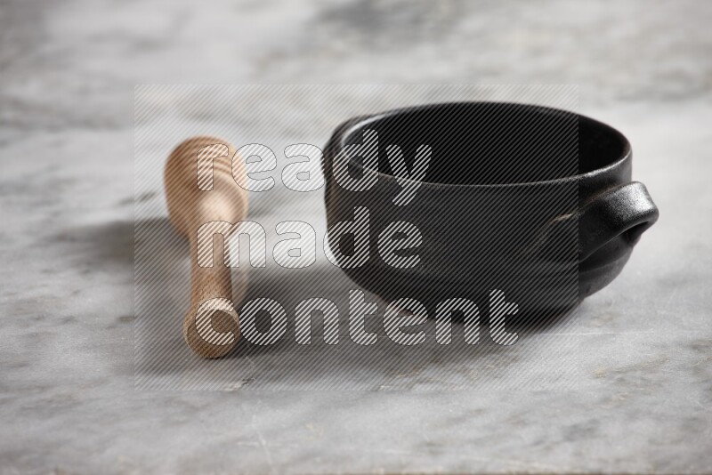 Black pottery bowl with wooden honey dipper on the side on grey marble background