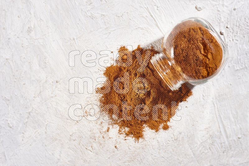 A glass jar full of ground paprika powder flipped with some spilling powder on white background