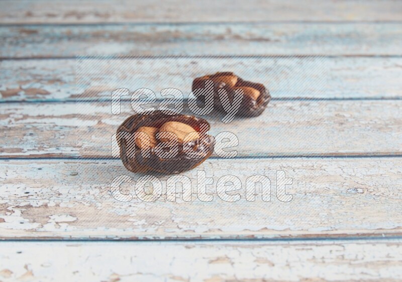 two almond stuffed madjoul dates on a light blue wooden background