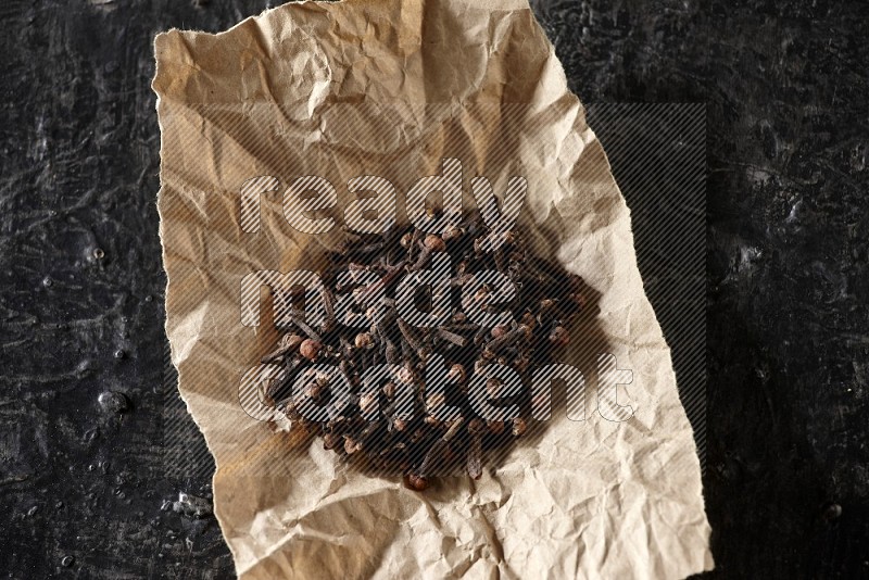 Cloves in crumpled piece of paper on a textured black flooring