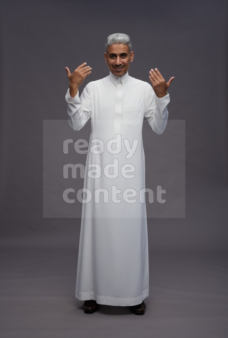 Saudi man wearing thob standing interacting with the camera on gray background
