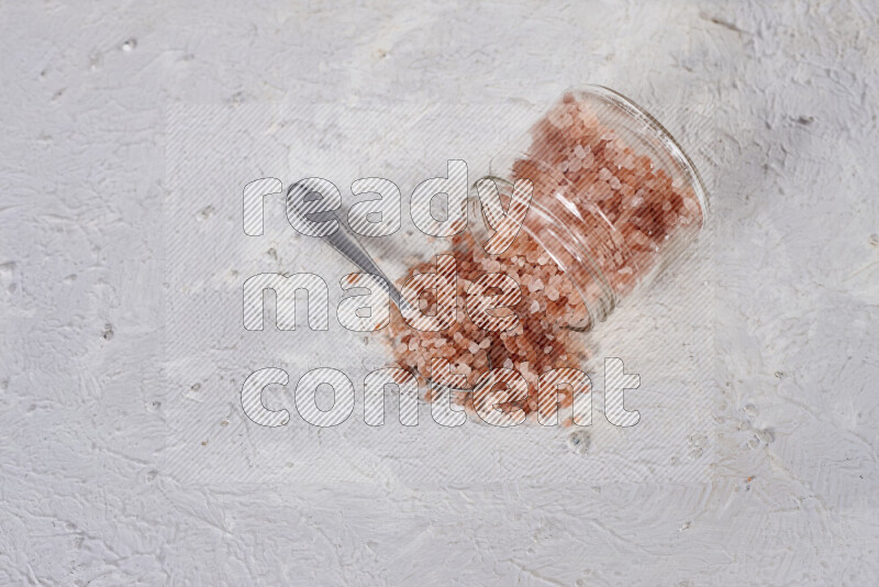 A glass jar full of coarse himalayan salt crystals on white background