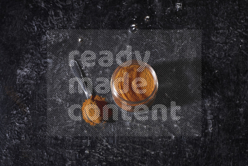 A glass jar full of ground paprika powder on black background