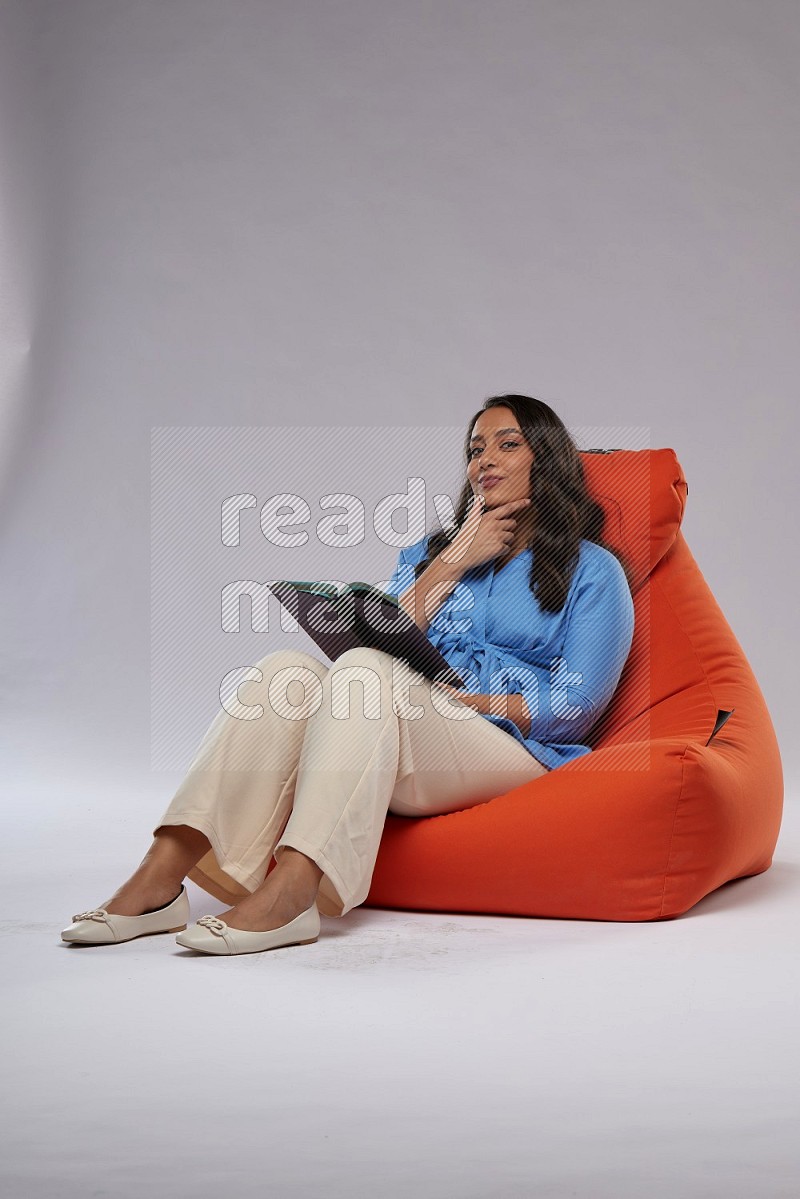 A woman sitting on an orange beanbag and reading a book