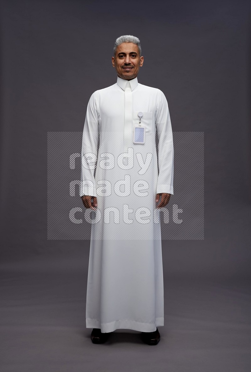 Saudi man wearing thob with pocket employee badge standing interacting with the camera on gray background