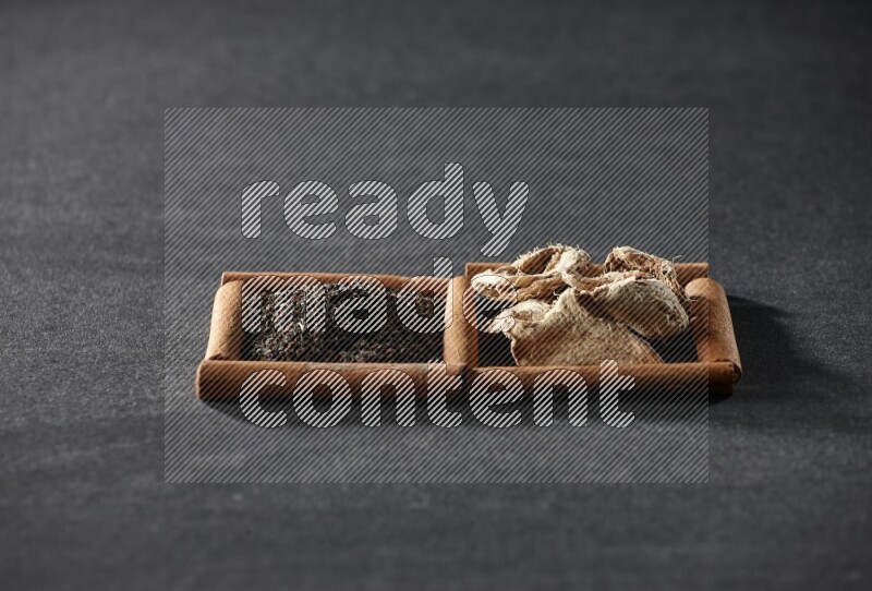 مربعان من أعواد القرفة ممتلئان بالزنجبيل المجفف والشاي الأسود علي خلفية سوداء