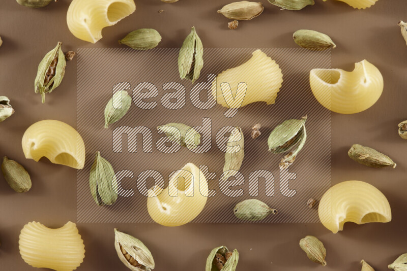 Raw pasta with different ingredients such as cherry tomatoes, garlic, onions, red chilis, black pepper, white pepper, bay laurel leaves, rosemary and cardamom on beige background