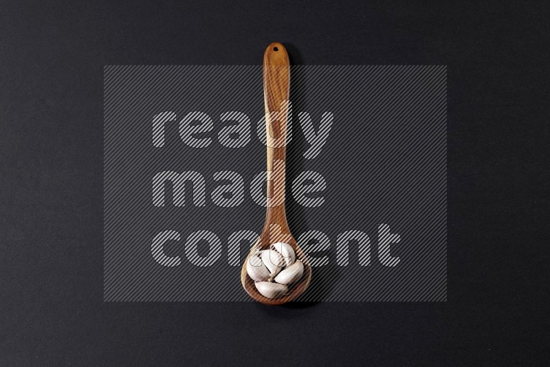 A wooden ladle full of garlic cloves on a black flooring in different angles
